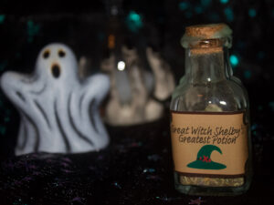 A product photo of a spell jar with the label "Great Witch Shelby's Greatest Potion" in the right background is a ceramic ghost and hourglass.